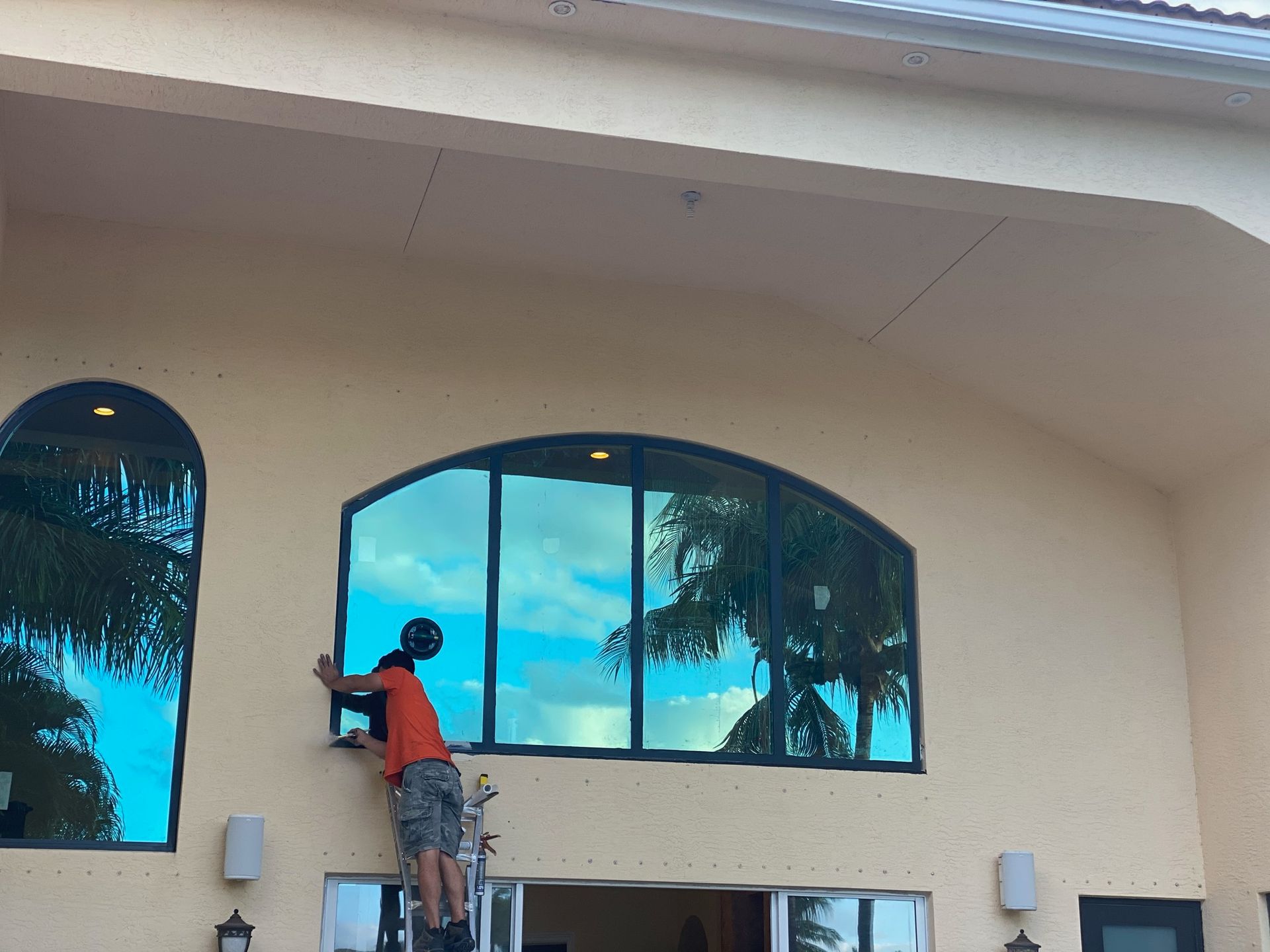 A man is standing on a ladder cleaning a large window.