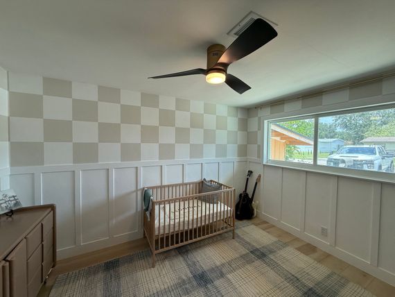 A nursery with custom carpentry, a crib, checkerboard accent wall, and a ceiling fan.