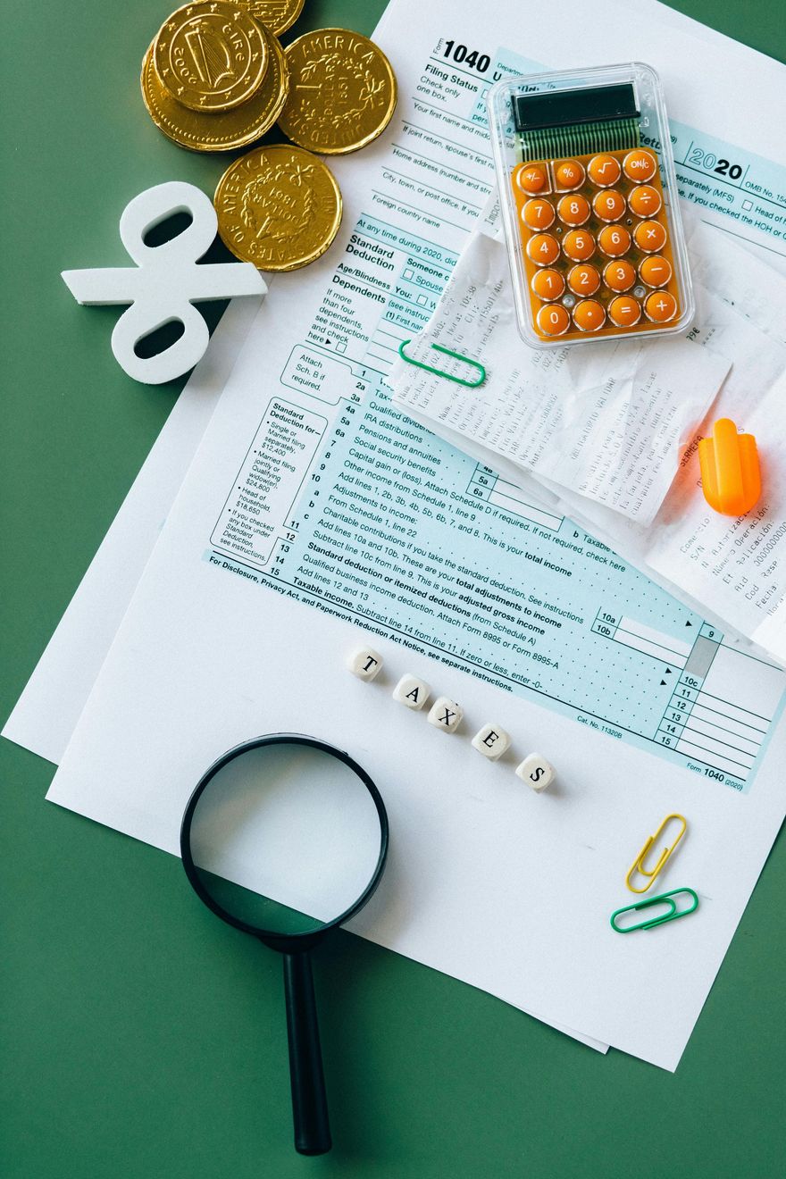 Tax form 1040, gold coins, a percent symbol, a calculator, a magnifying glass, and paper clips on a green background.