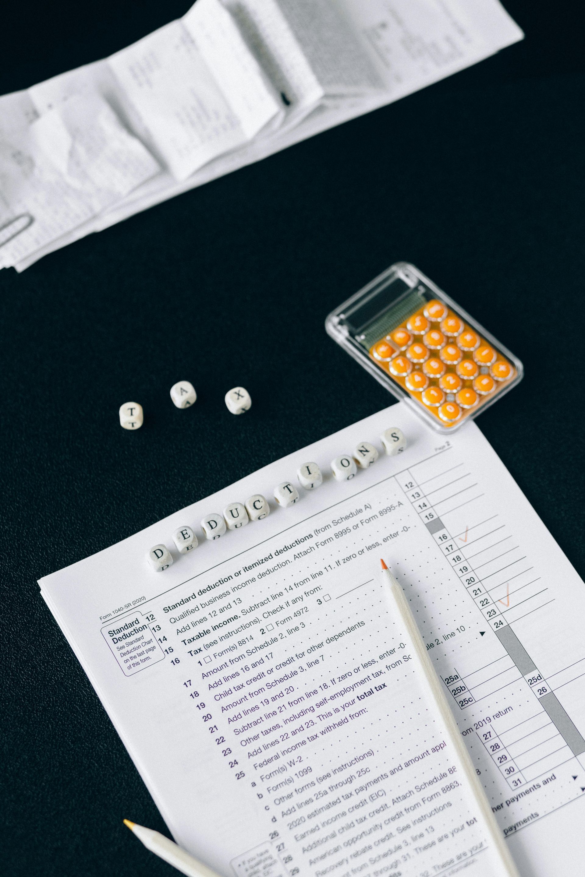 A flat-lay of a tax form, receipts, a calculator, and small dice arranged to spell 