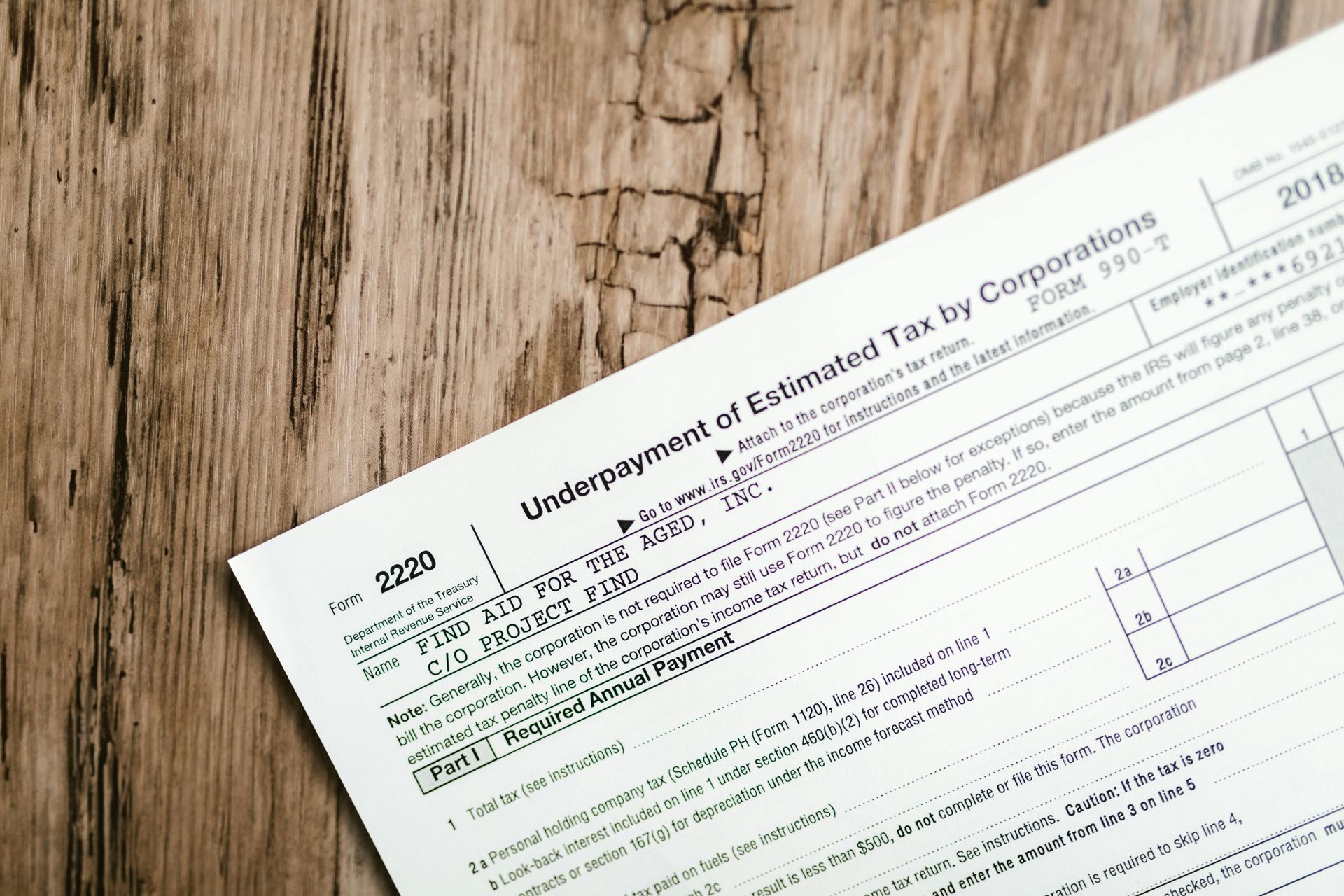A close-up of a 2018 IRS Form 2220 for the underpayment of estimated tax by corporations, resting on a wooden surface.