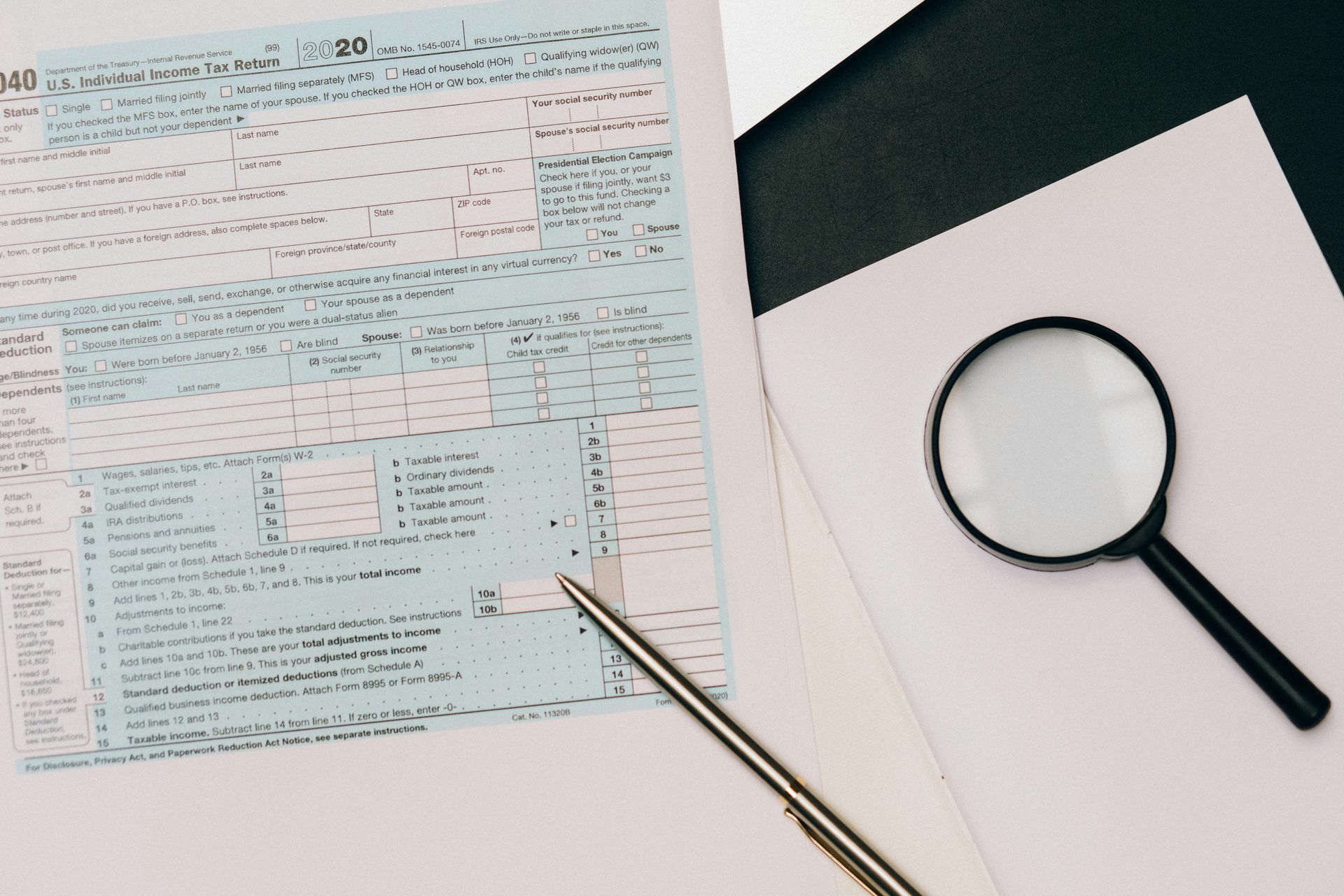 A magnifying glass and a pen lie on a tax form, symbolizing document review and financial preparation.