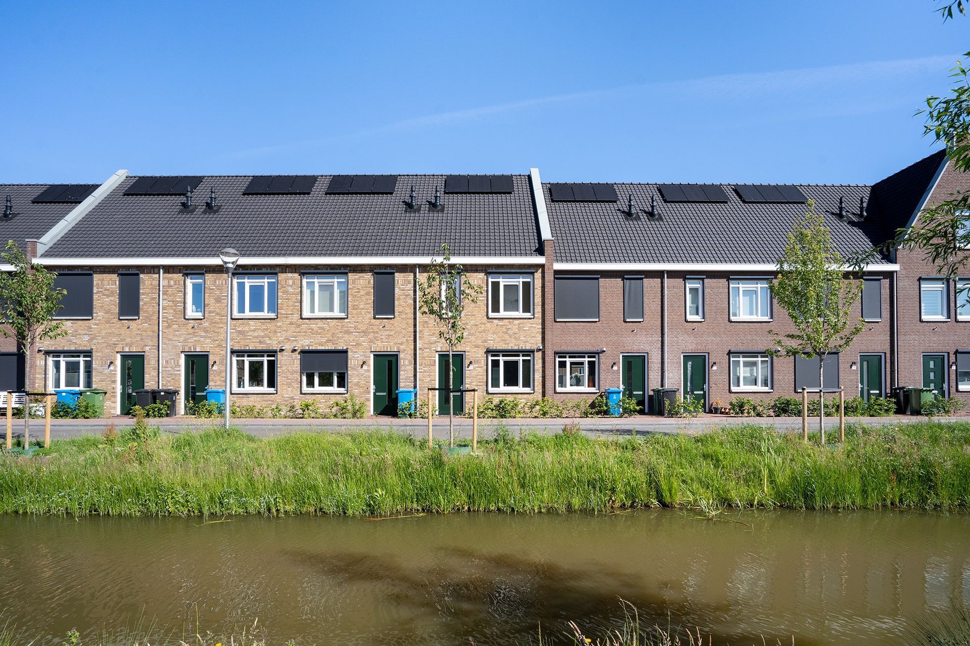 Rij rijtjeshuizen met zonnepanelen op de daken, langs een kanaal.