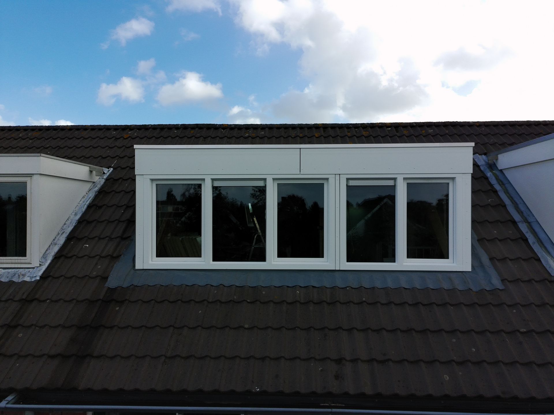 Witte kozijnen in een donker pannendak, onder een blauwe hemel met wolken.