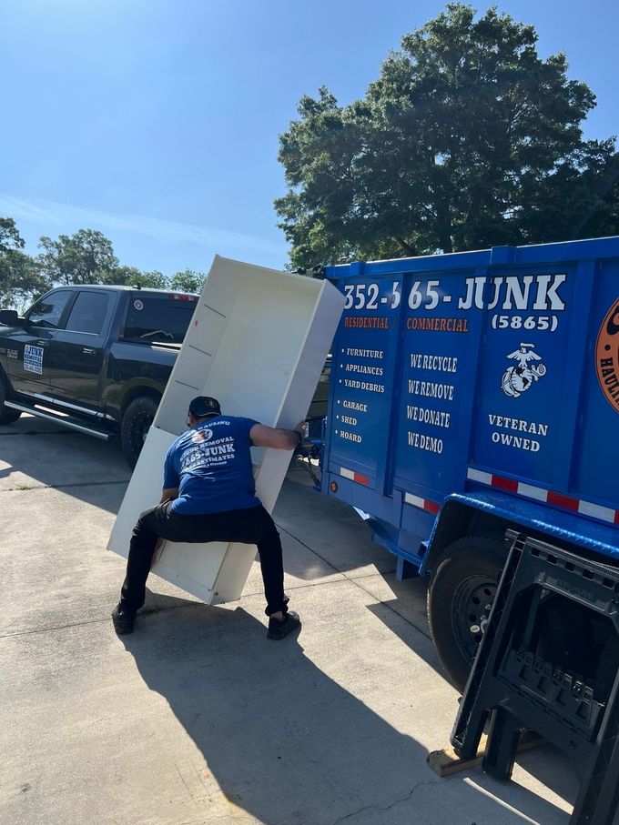 Two people carrying a white cabinet out of a brick building's doorway. Two people carrying a white cabinet out of a brick building's doorway.
