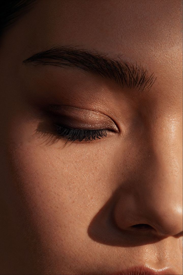 Close-up of a face with closed eyes, glittery eye makeup, and a nose in warm light