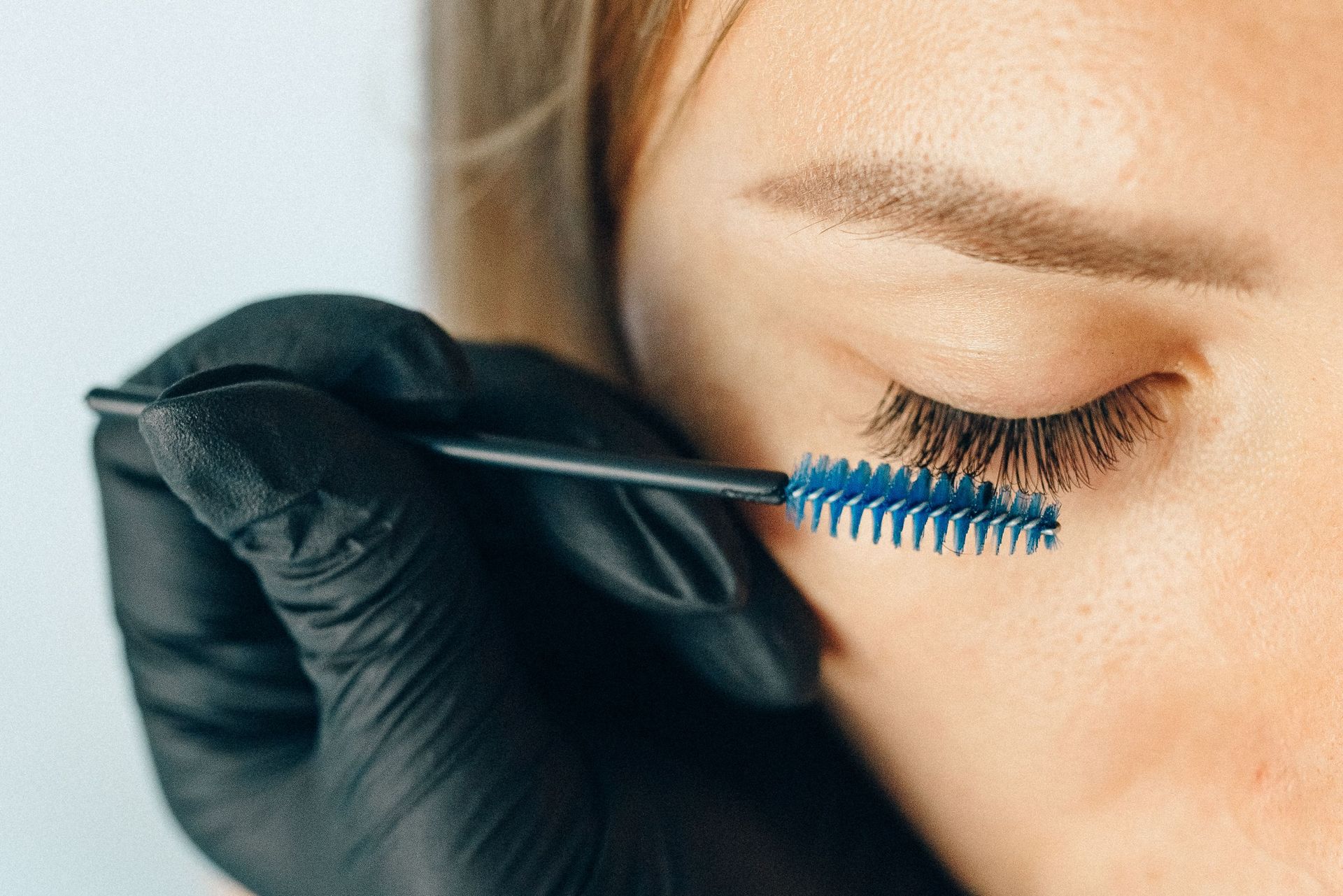 Gloved hand applying blue mascara to a closed eye with long lashes