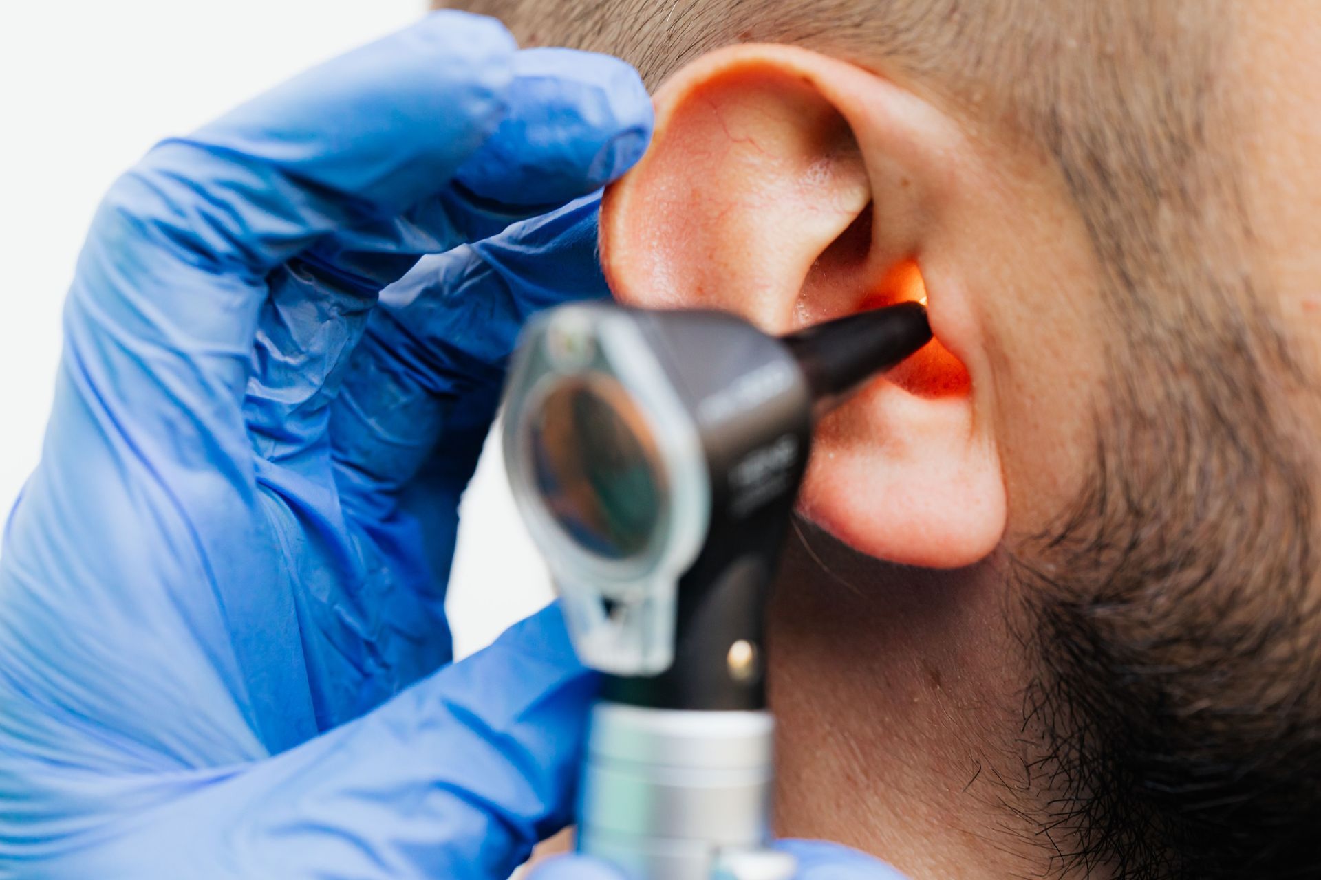 Doctor examining ear with an otoscope while wearing blue gloves