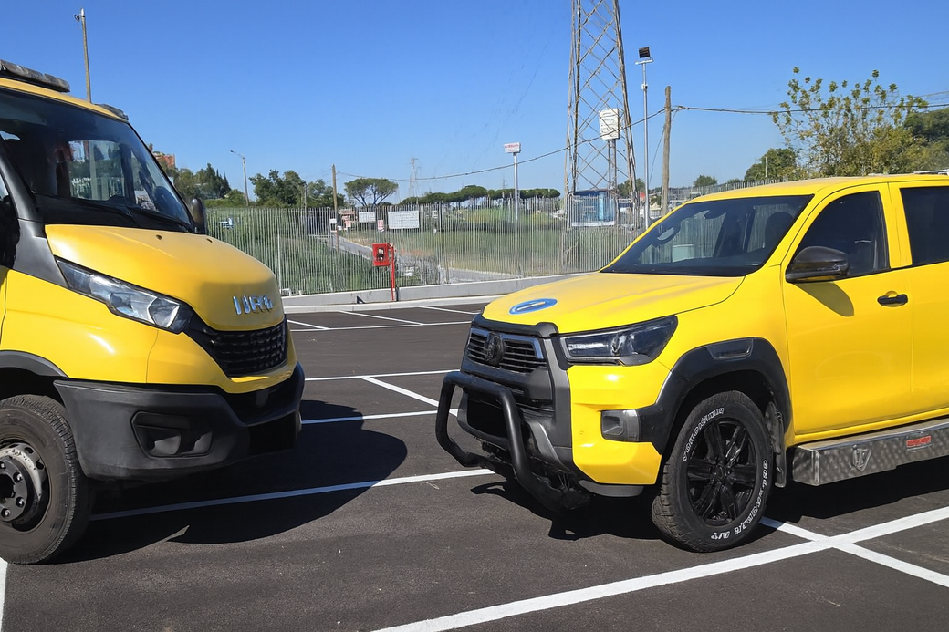 Furgone e camion gialli parcheggiati in un parcheggio. I veicoli sono sotto un cielo azzurro, in una giornata di sole.