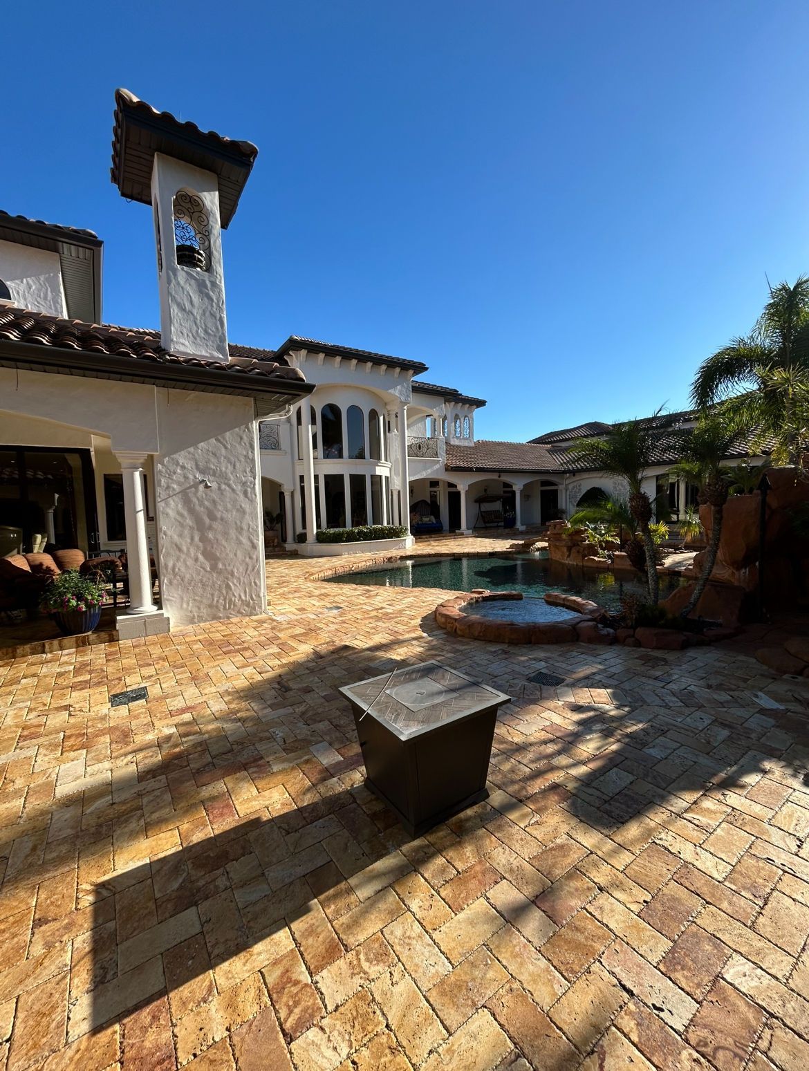 Luxurious house with a pool, brick patio, and clear blue sky.