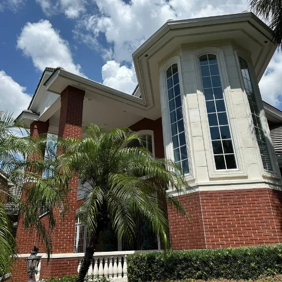 Two-story brick and stone house with arched windows, a palm tree, and a blue sky.