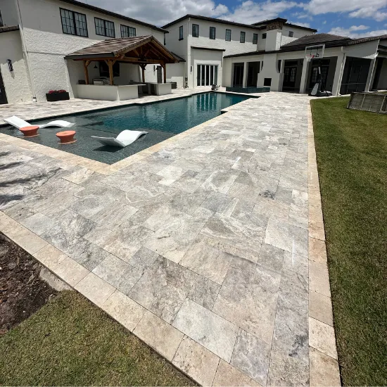 A luxury backyard with a pool and stone patio, overlooking a large house.