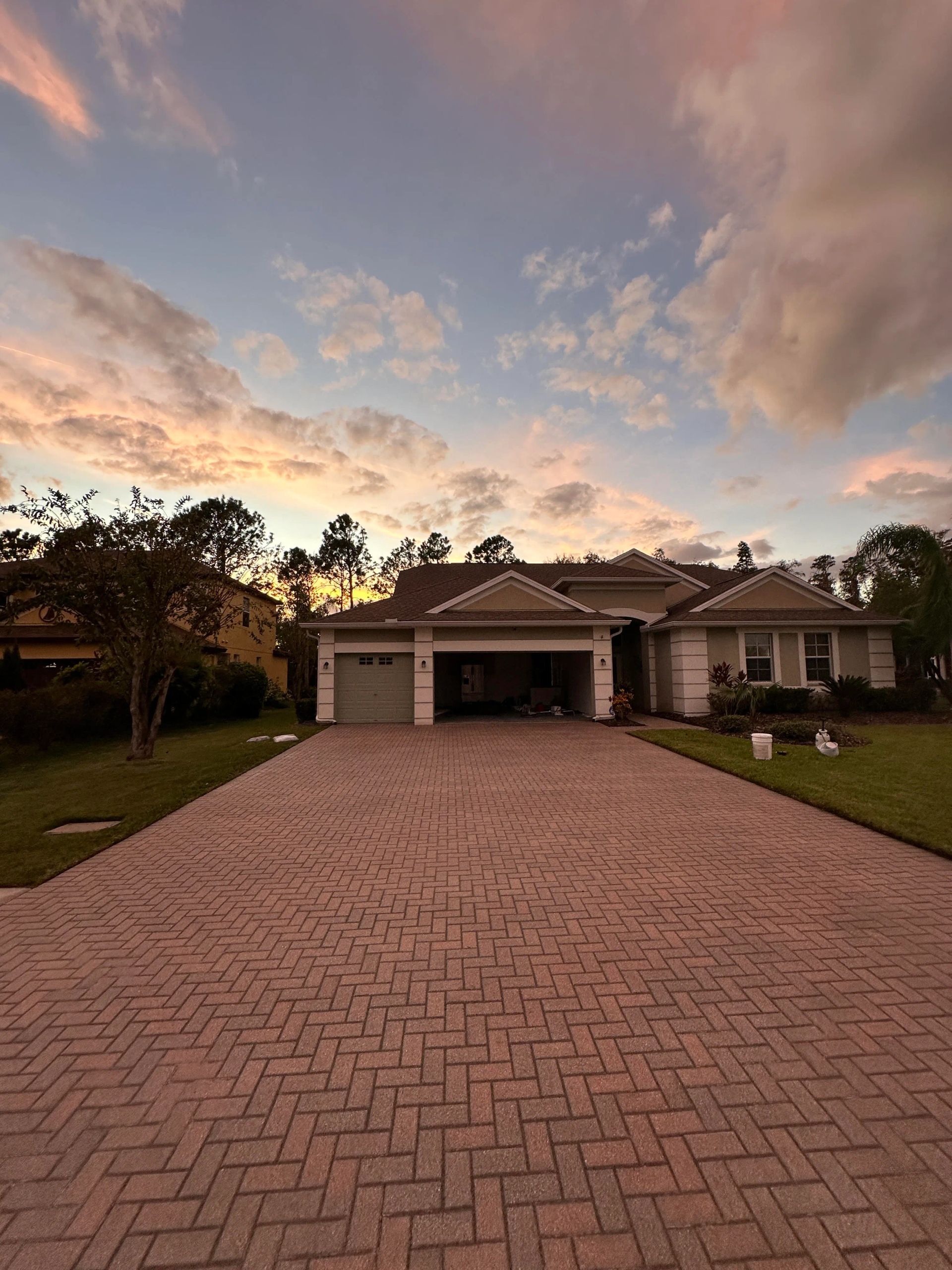 House with red brick driveway under a sunset sky with clouds.