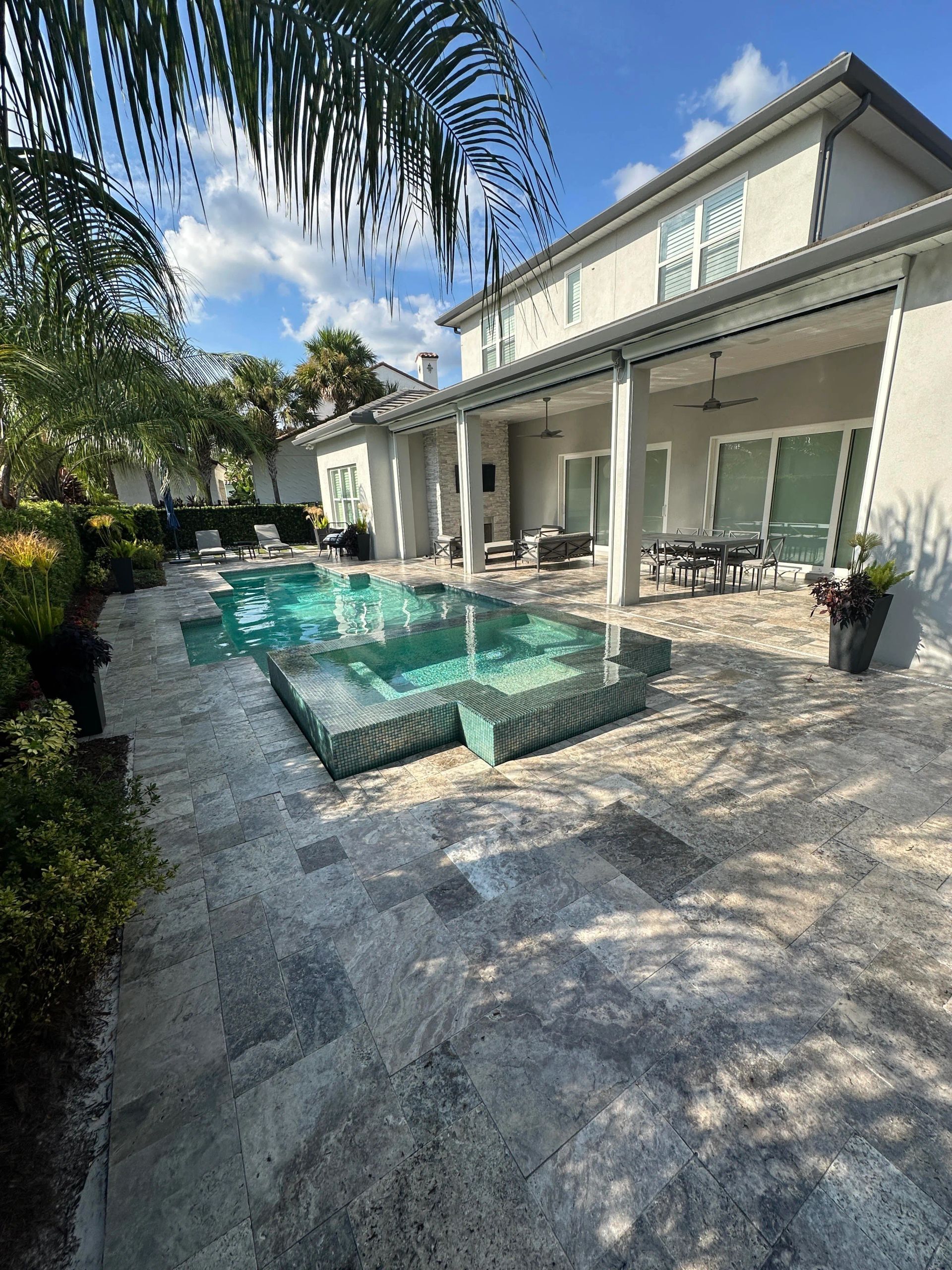 Backyard with a swimming pool, steps, and patio, adjacent to a two-story house with a blue sky overhead.