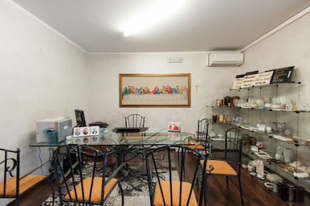 Piccola stanza con tavolo in vetro, mensole espositive e ricamo raffigurante l'Ultima Cena.