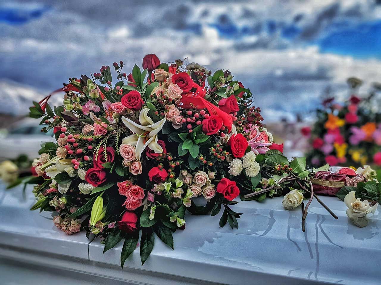 Large Red, Pink, And White Funeral Flower Arrangement Displayed Outdoors On A Casket Or Hearse