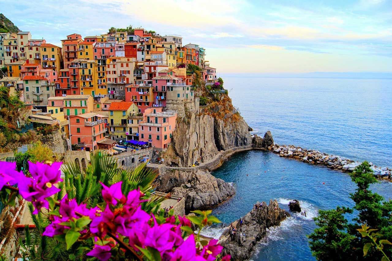 Colorful Cliffside Village over Blue Coastal Harbor with Flowers in Foreground