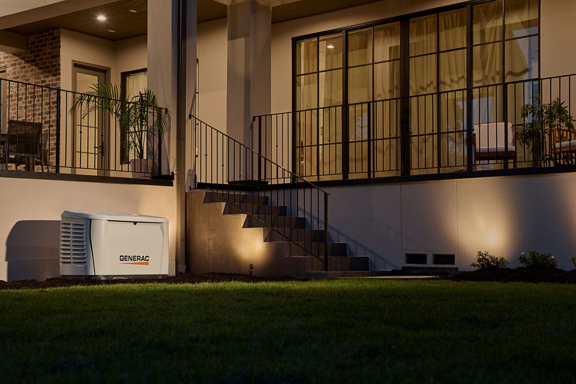 A Generac home standby generator installed on a grassy lawn next to the steps of a modern house at night.