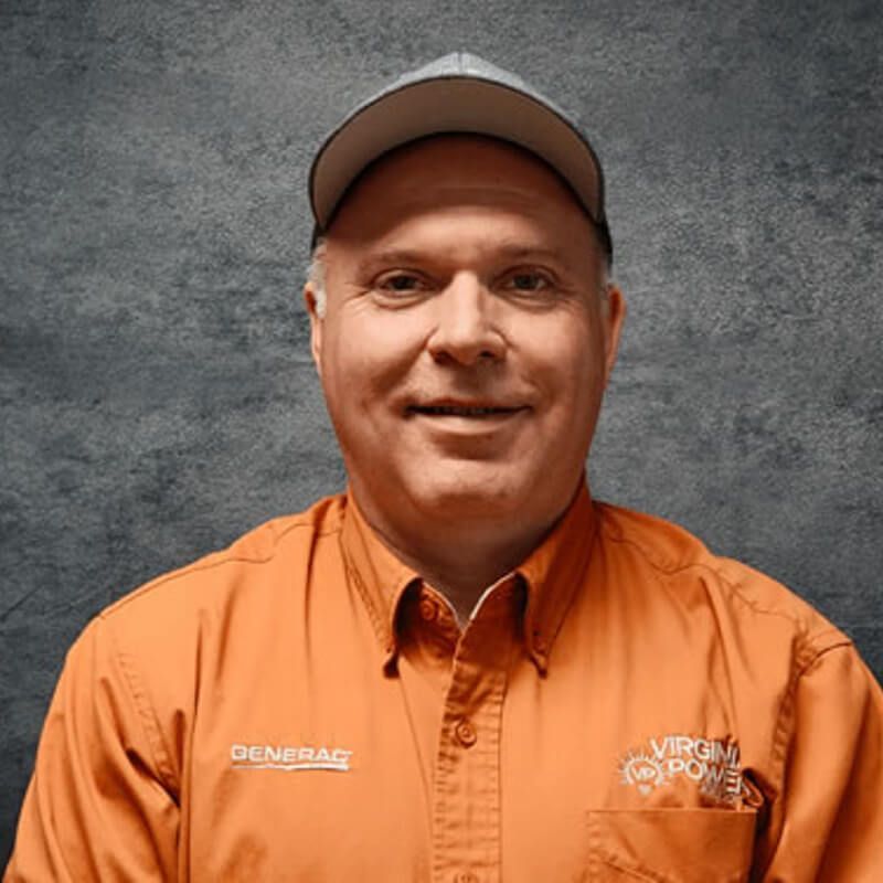 Man in orange work shirt and cap, smiling in front of a gray backdrop.