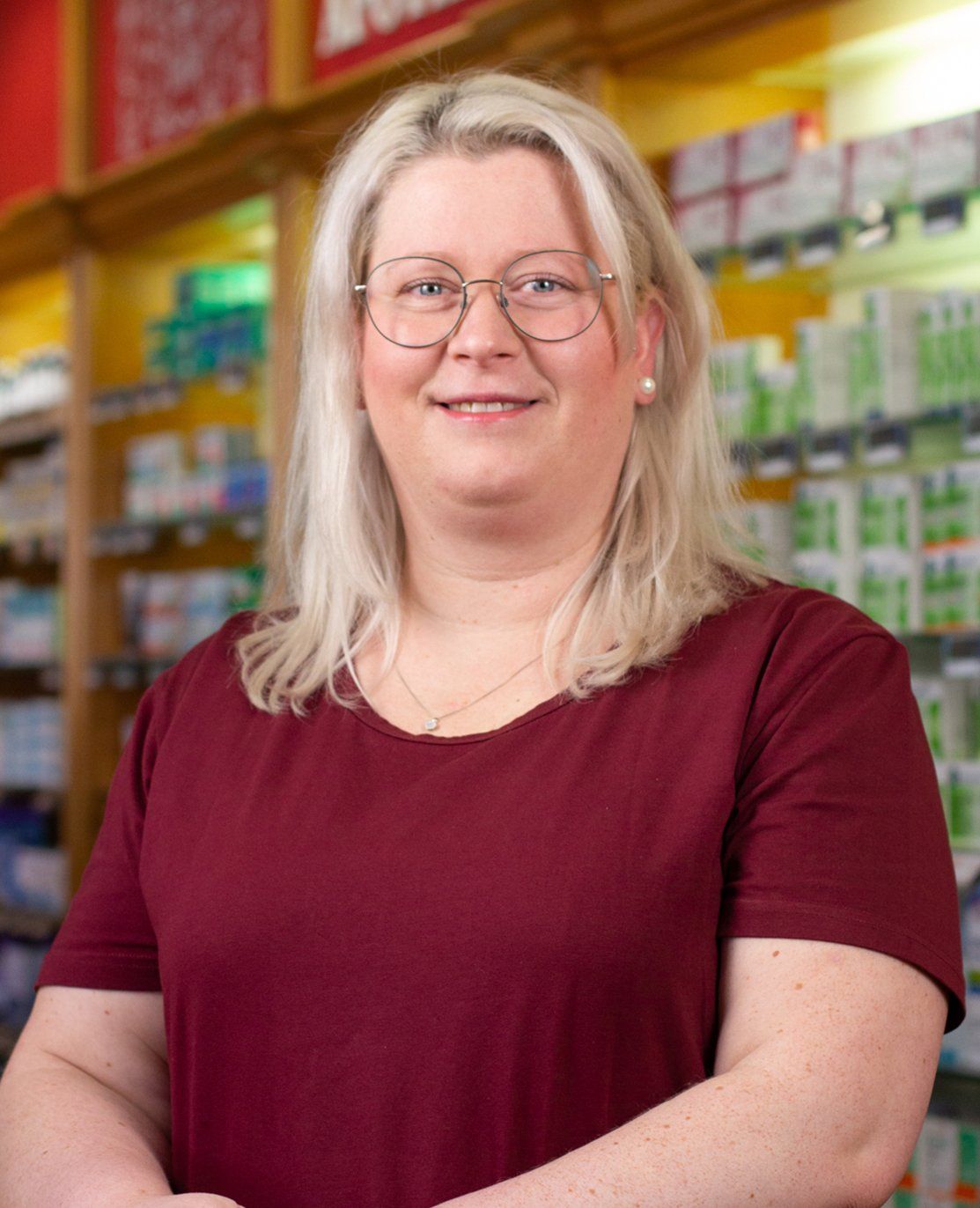 Eine Frau mit Brille und kastanienbraunem Hemd steht in einer Apotheke.