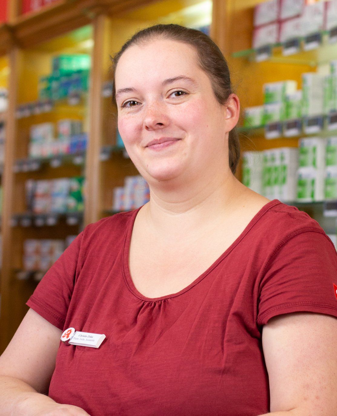 Eine Frau in einem roten Hemd lächelt vor einem Apothekenregal