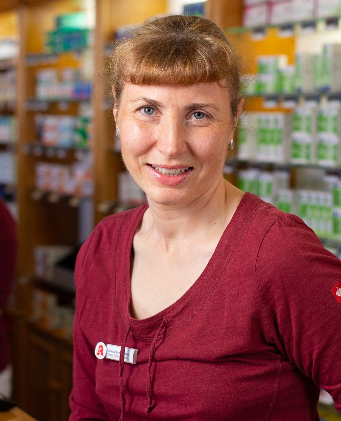 Eine Frau in einem roten Hemd lächelt in einer Apotheke.