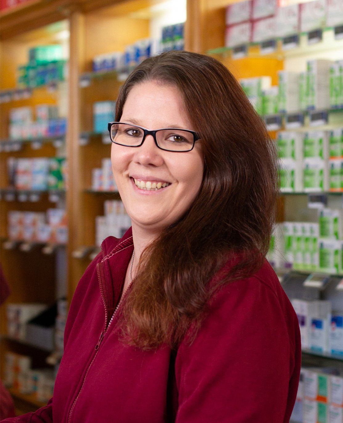 Eine Frau mit Brille lächelt in einer Apotheke.