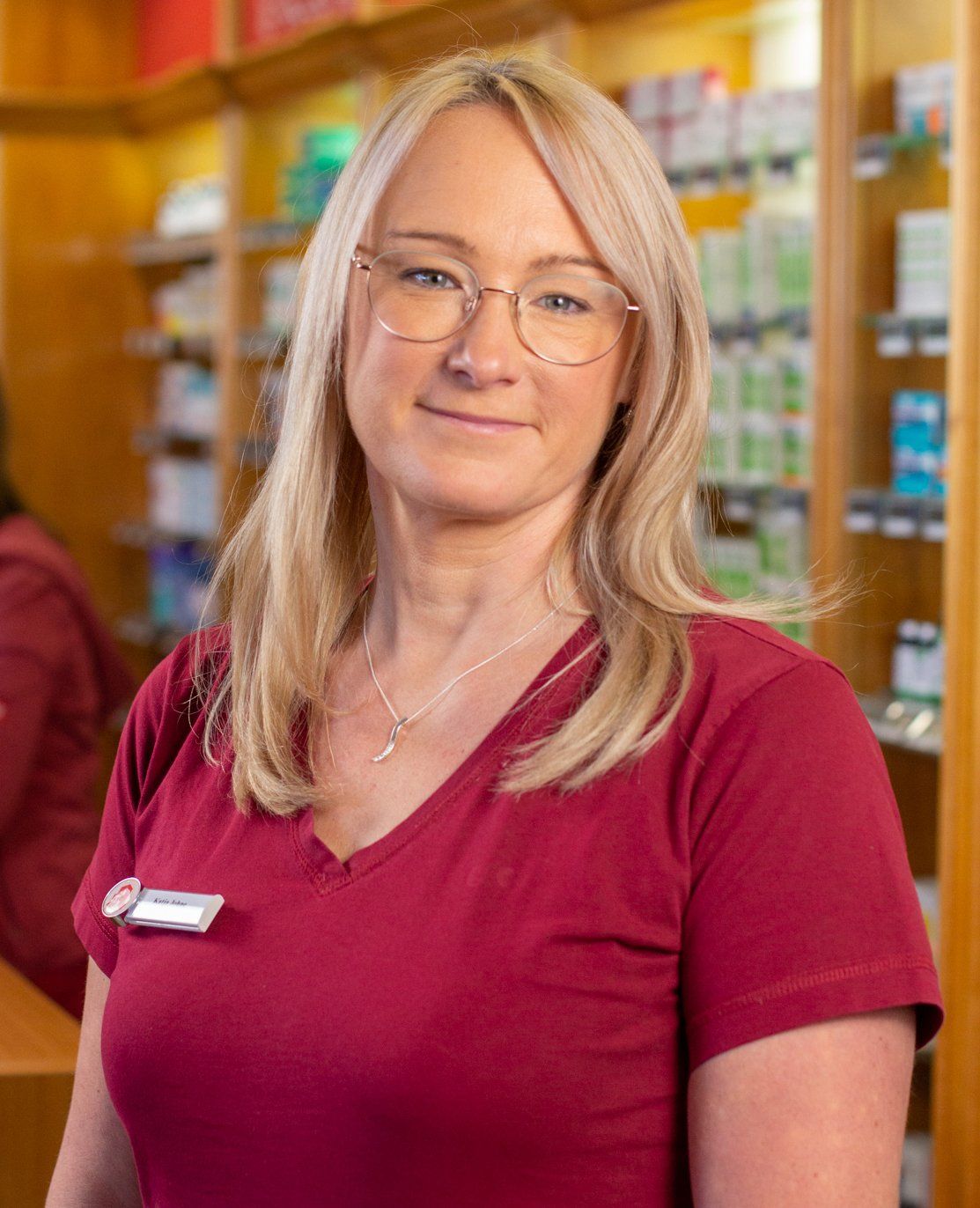 Eine Frau mit Brille und rotem Hemd steht in einer Apotheke.