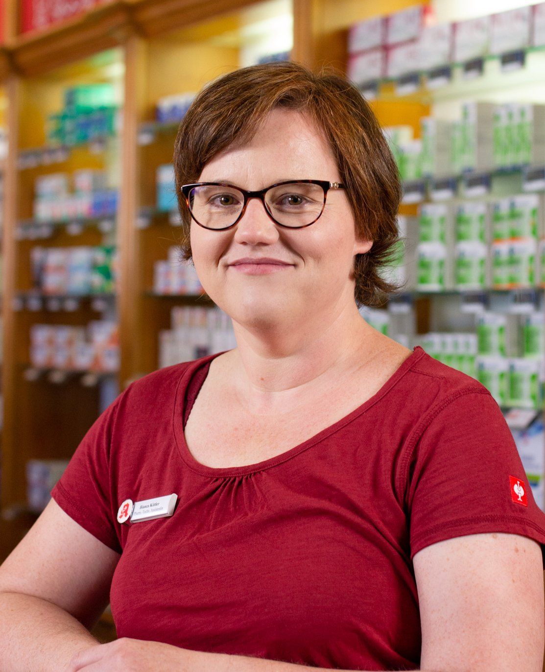 Eine Frau mit Brille und rotem Hemd steht in einer Apotheke.