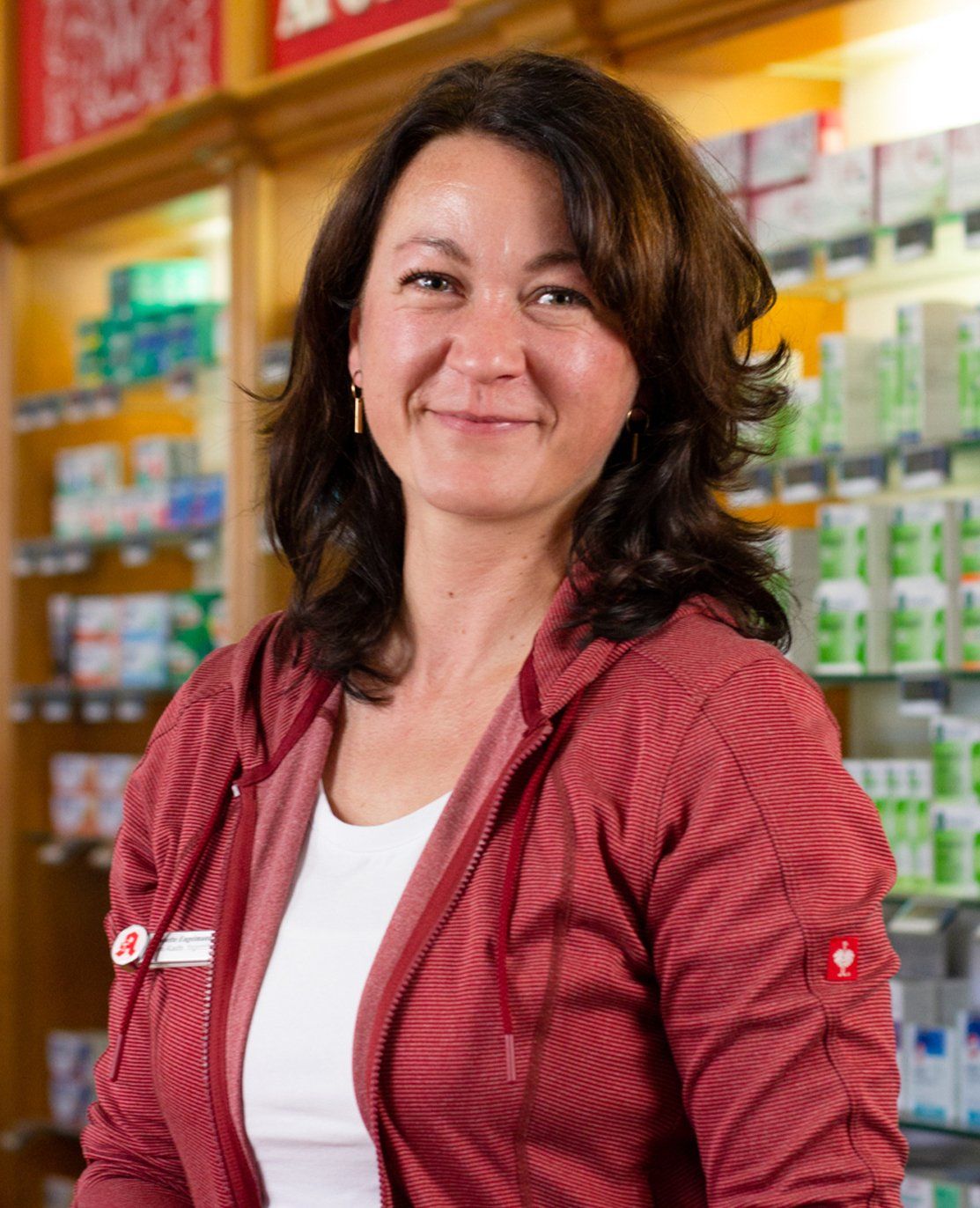 Eine Frau in einer roten Jacke steht vor einer Apotheke.