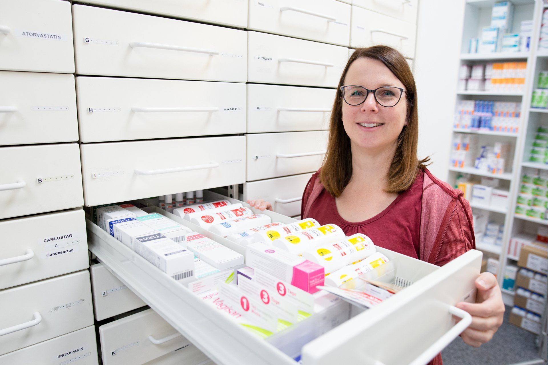 Eine Frau hält in einer Apotheke eine Schublade voller Pillen.