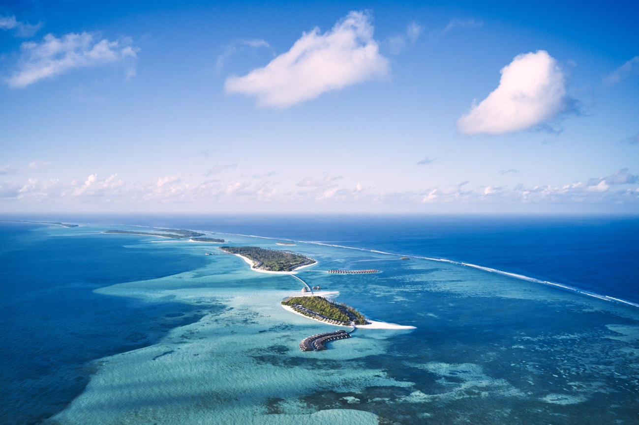 Aerial view of a chain of small islands in turquoise water under a blue sky with fluffy clouds.