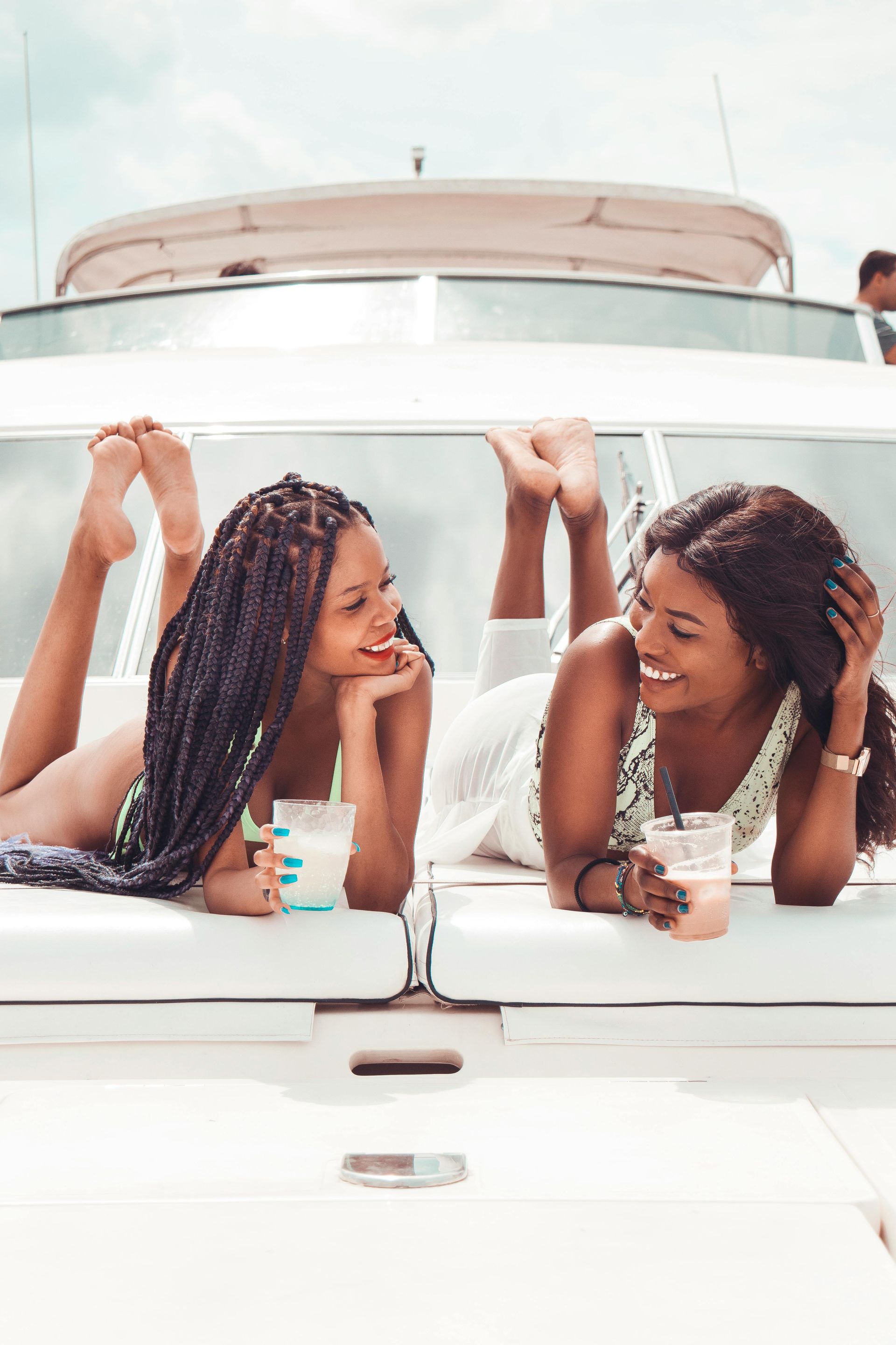 Two women lounging on a yacht, smiling and drinking cocktails on a sunny day.
