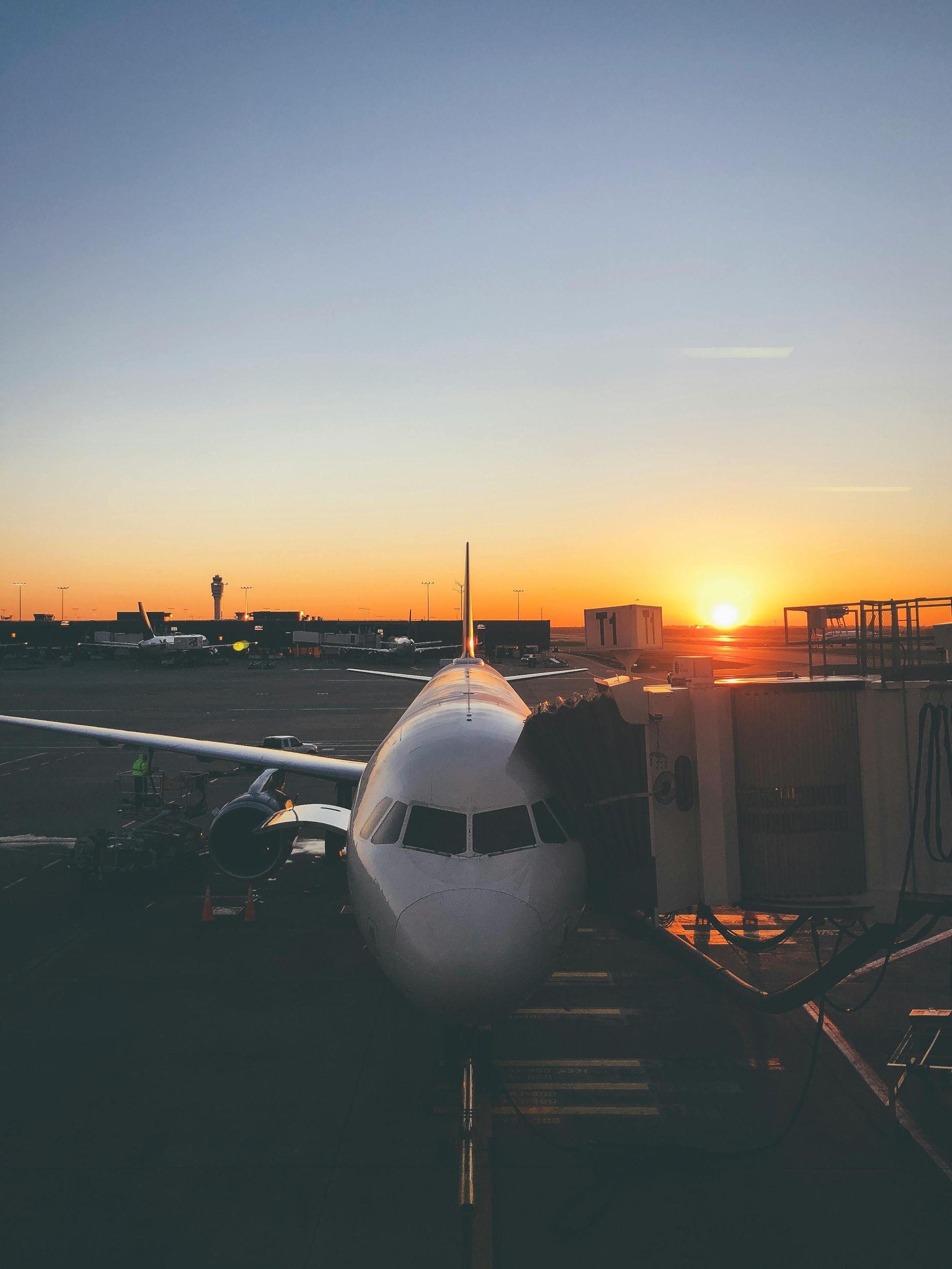 Airplane at gate, sunset background, orange and blue sky, airport setting.