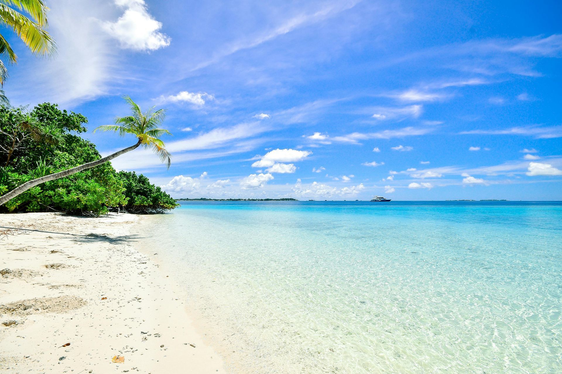 Beach with white sand, turquoise water, palm trees, and a bright blue sky with wispy clouds.