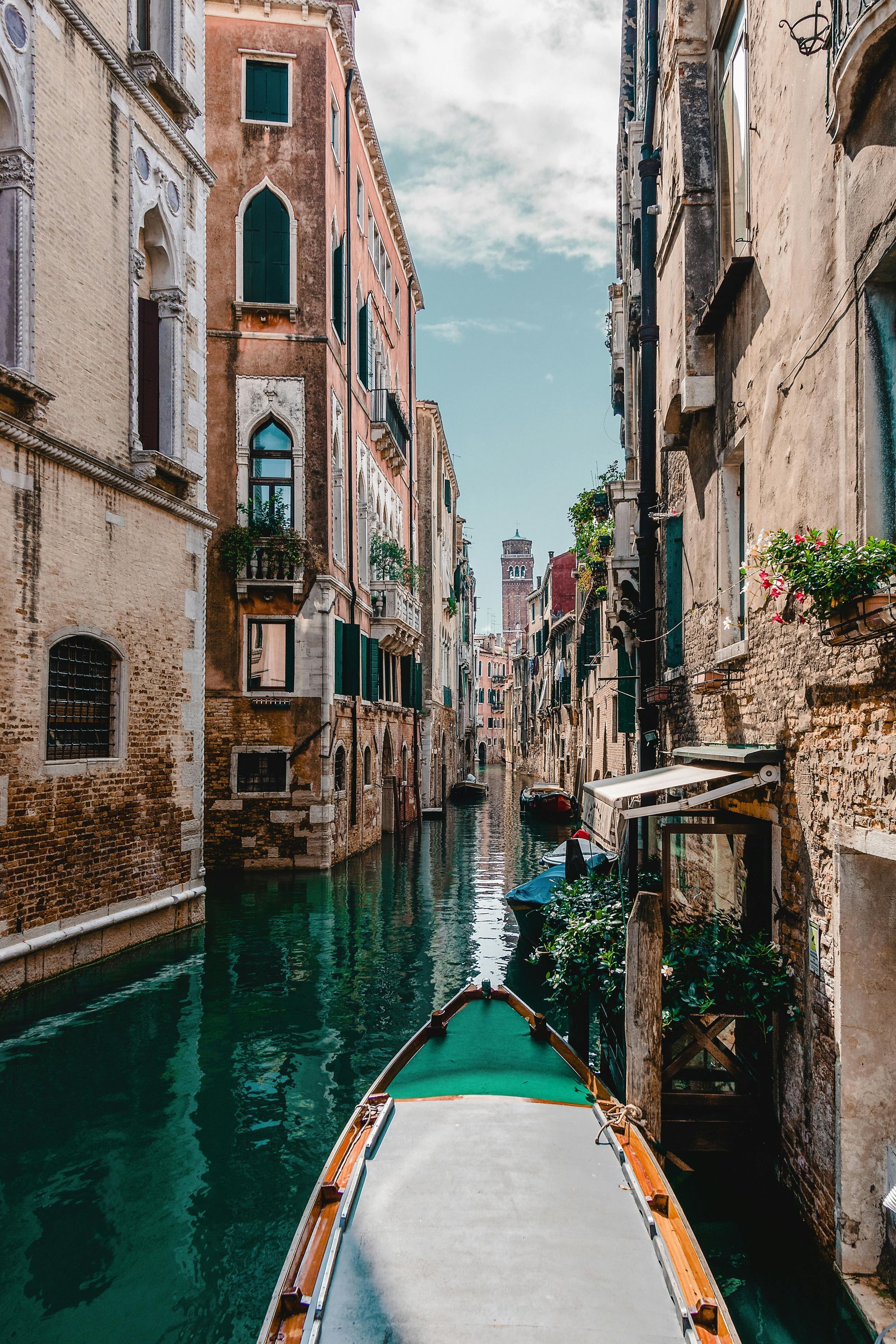 A gondola glides through a Venetian canal, lined by aged buildings under a blue sky.
