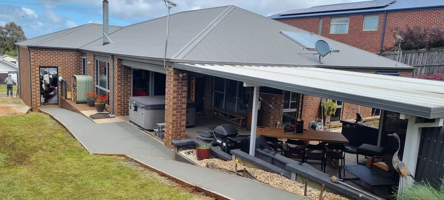 A brick house with a gray roof and a long concrete ramp. A patio with outdoor furniture extends from the house.