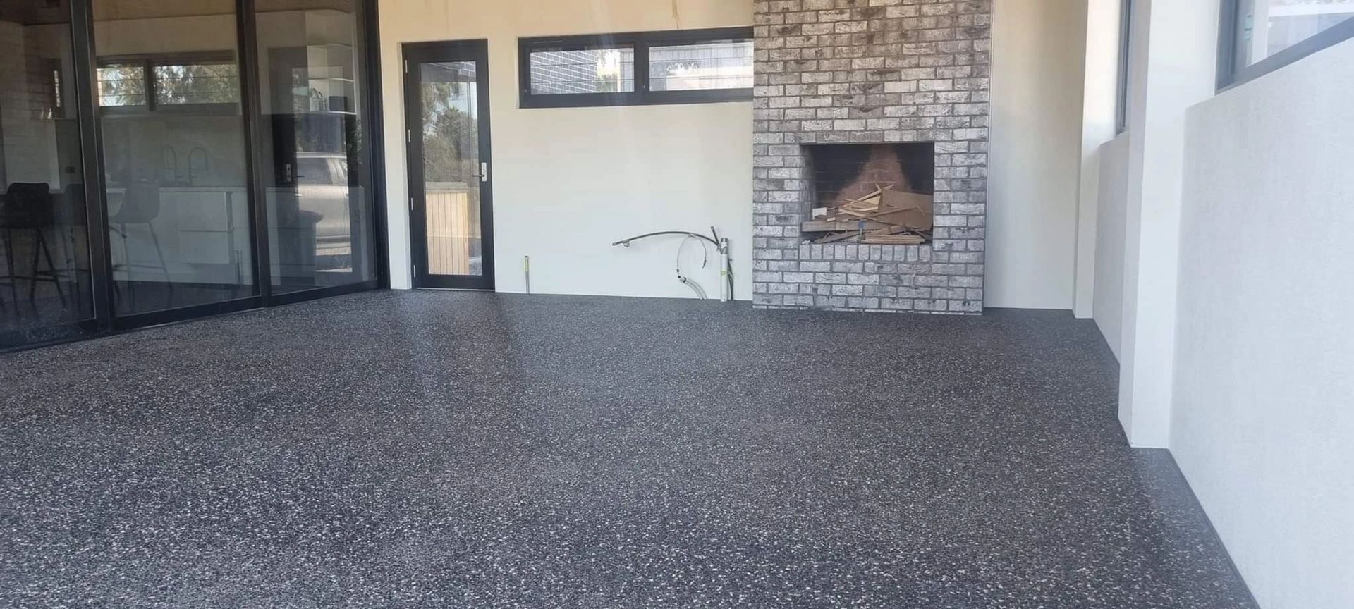 An outdoor patio with a pebble floor and a fireplace. There are glass sliding doors to the left and white walls.