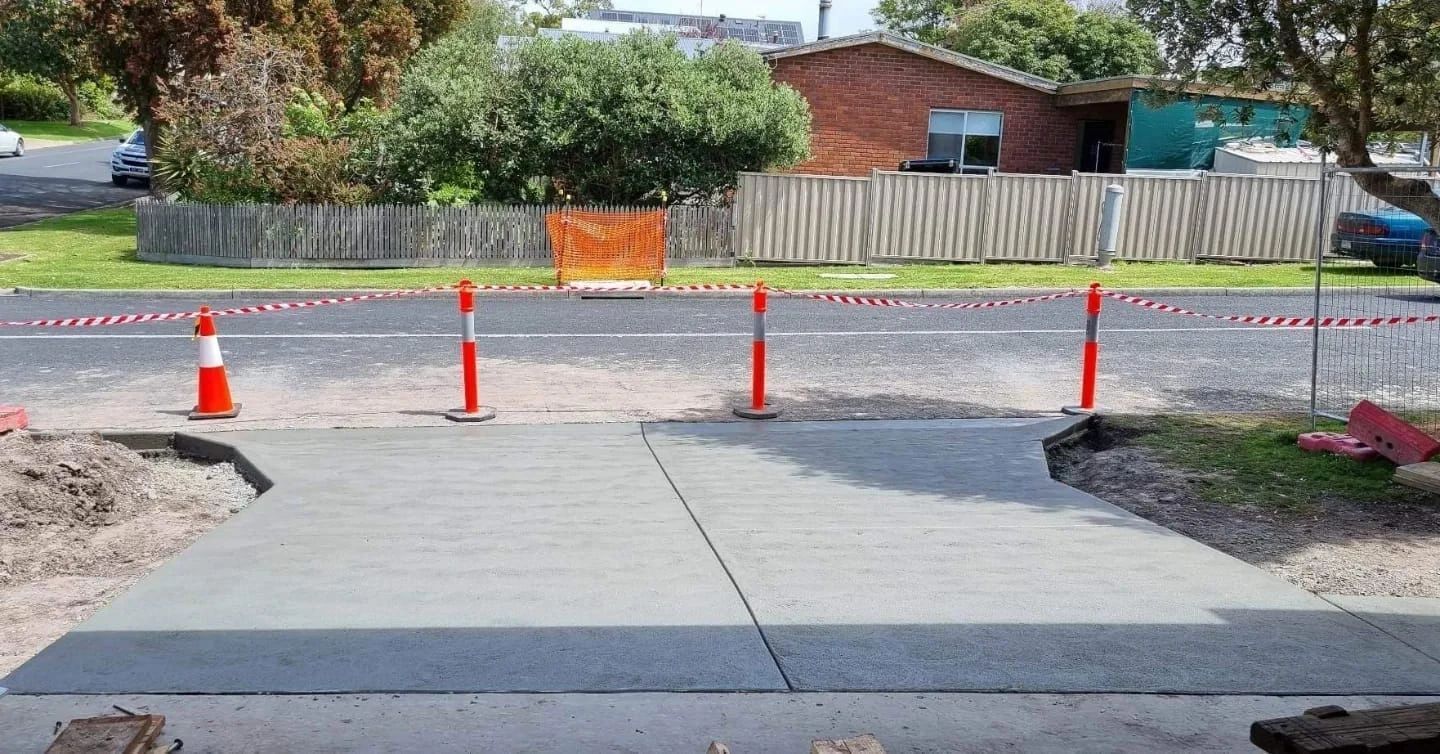 Newly poured concrete driveway section with orange traffic cones and caution tape blocking access to road work.