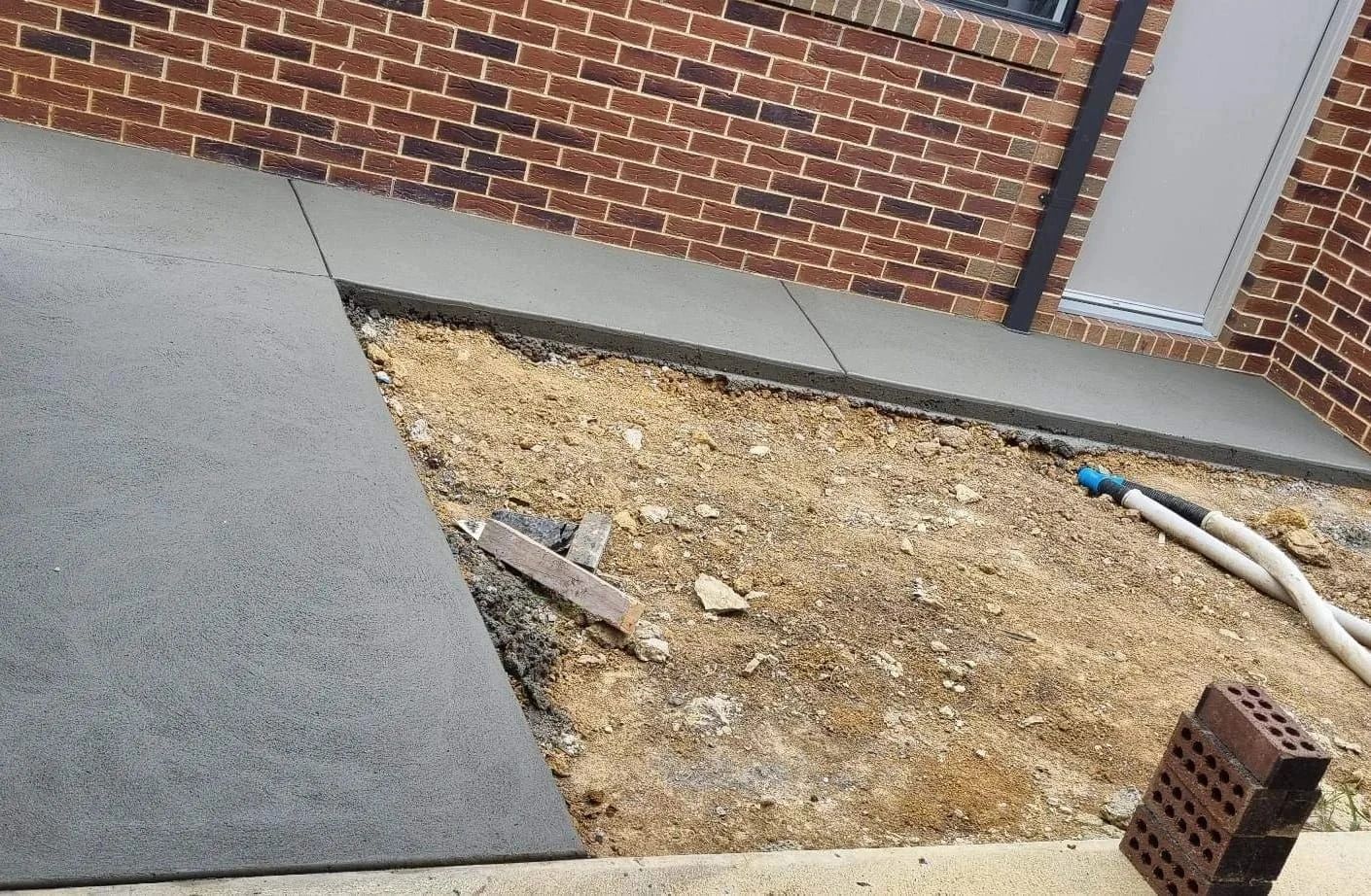 Brick building with a concrete walkway and gravel-filled space next to it. A small stack of bricks is on the right.