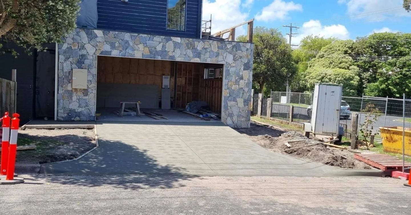 A garage with stone facade under construction, featuring an open doorway, new concrete driveway, and construction materials.