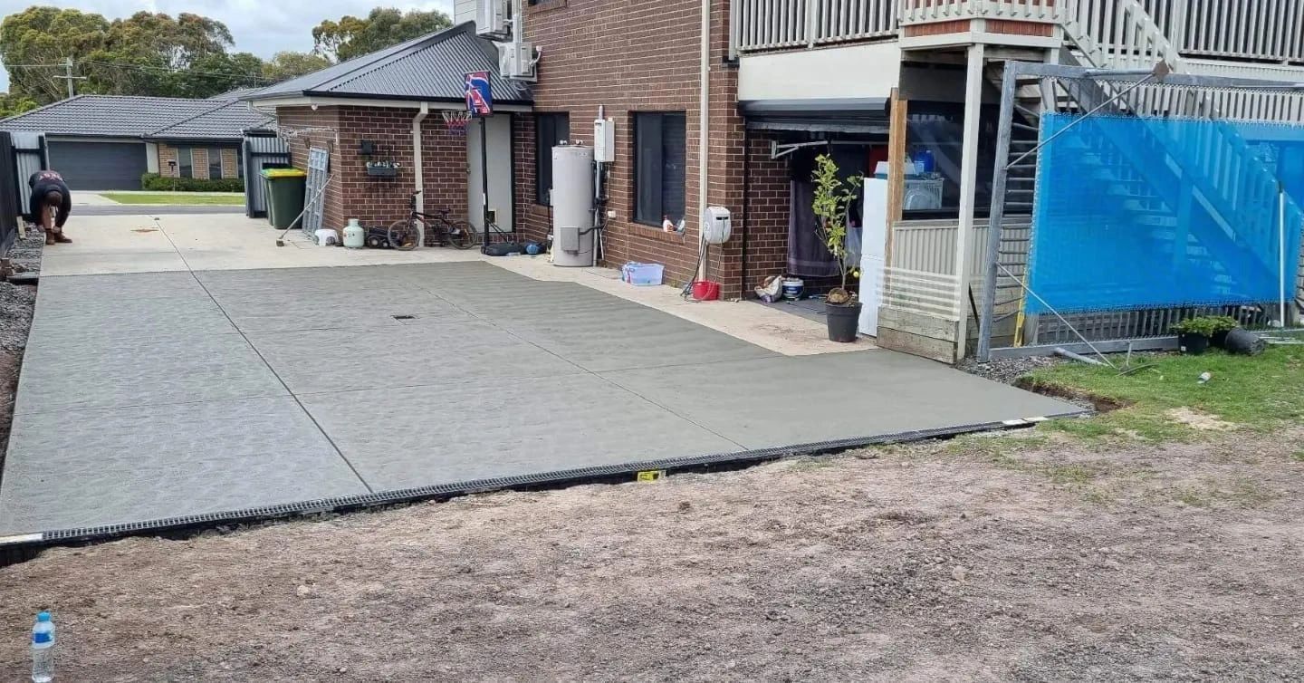 Freshly poured concrete driveway in front of a brick house, with construction materials and a grassy area in the foreground.