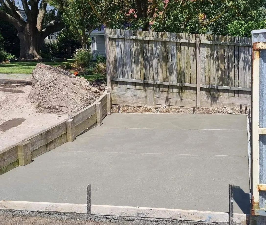 Freshly poured concrete slab within wooden borders, located in a fenced yard.
