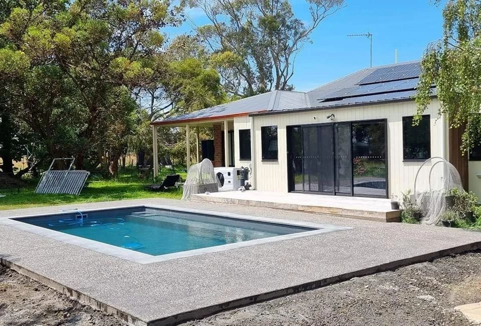 A garage with an open door, revealing tools inside. A concrete driveway leads to the garage, with grass and bushes on either side.