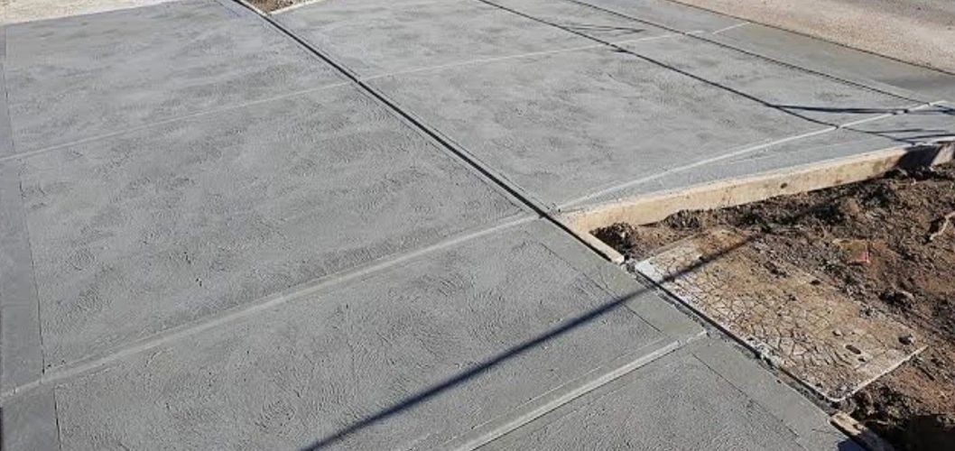 Newly poured concrete sidewalk with expansion joints; partially bordering dirt and grass.