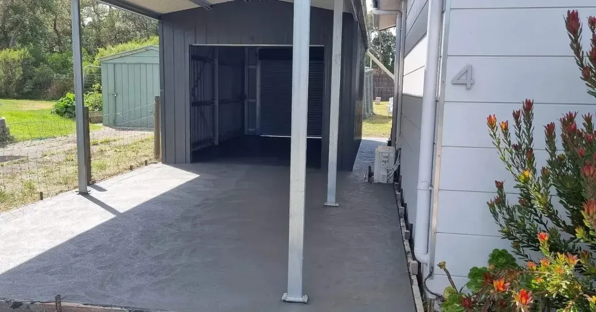 Workers pouring and smoothing concrete in an outdoor construction site. One person holds a chute, while another uses a large squeegee-like tool.
