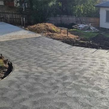 Dark gray stamped concrete driveway leading to a backyard with a wooden fence and house in the background.