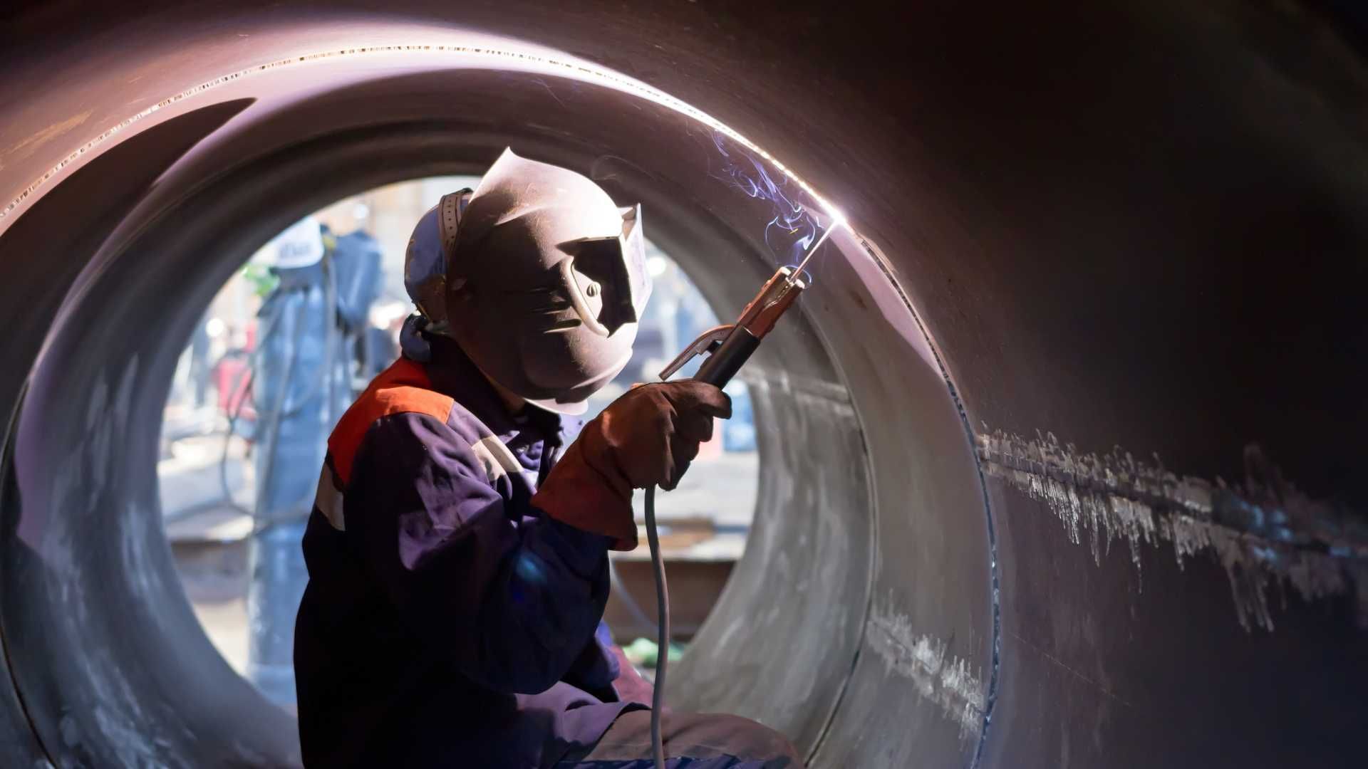 A man is welding a pipe in a factory.