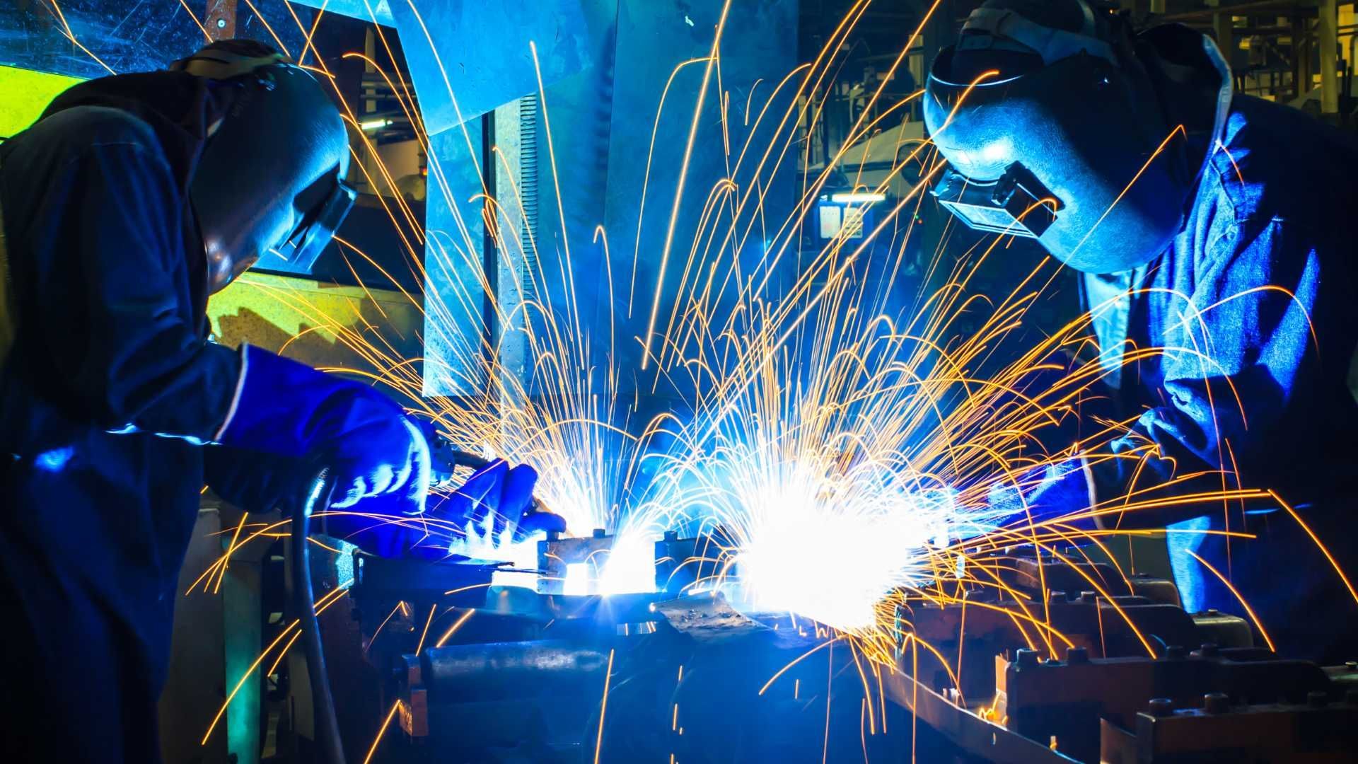 Two men are welding a piece of metal in a factory.