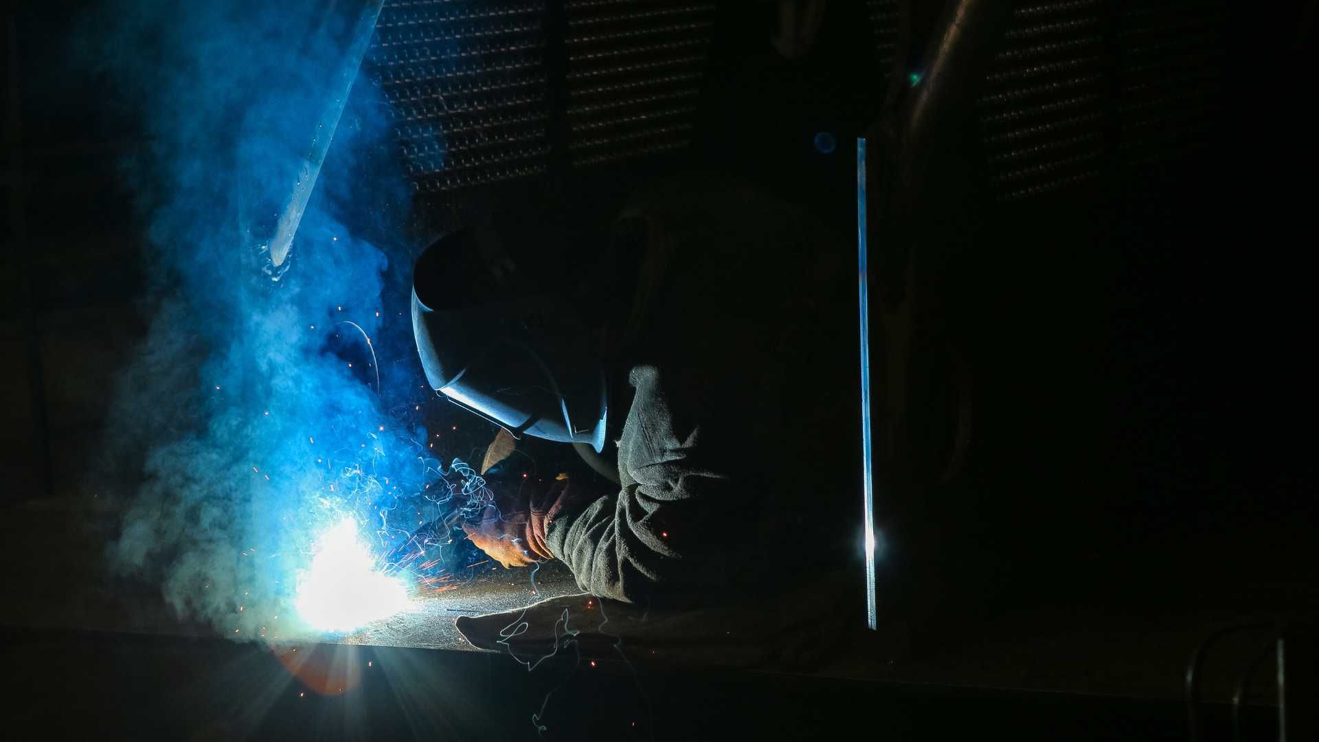 A man is welding a piece of metal in a dark room.